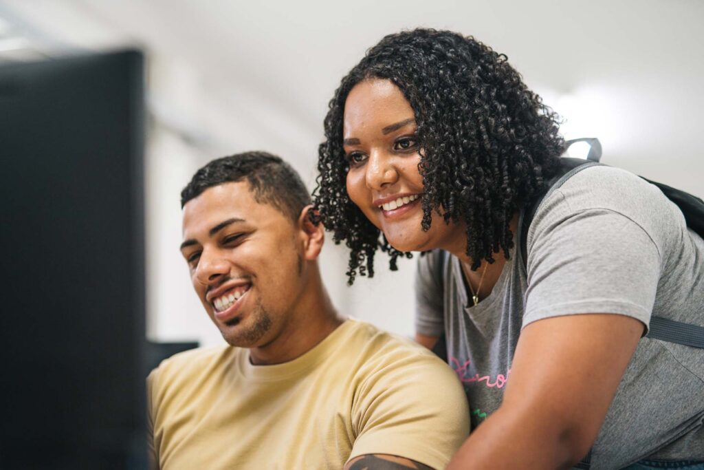 A young man and woman smiling while looking at a computer screen